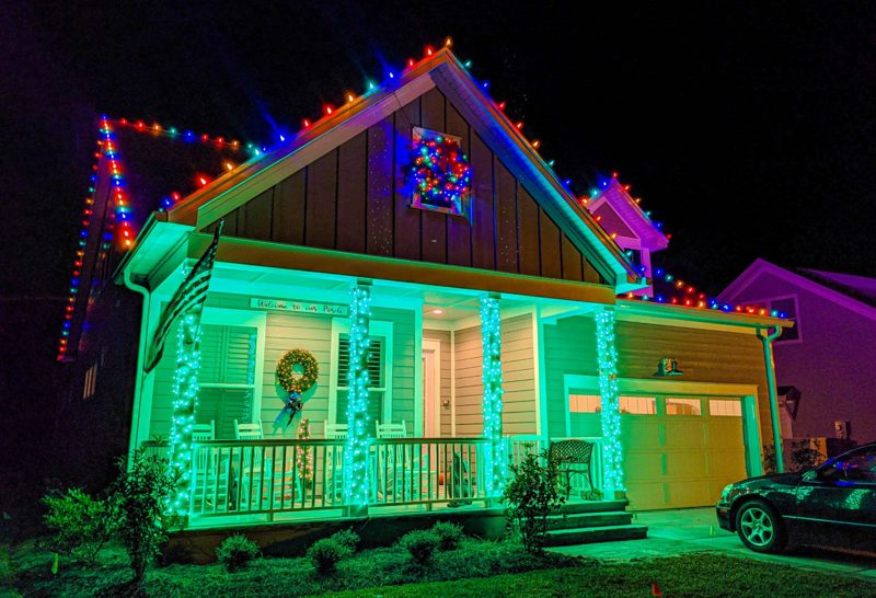 Craftsman home with multicolor roofline lights, a lit wreath and green-and-white wrapped porch columns