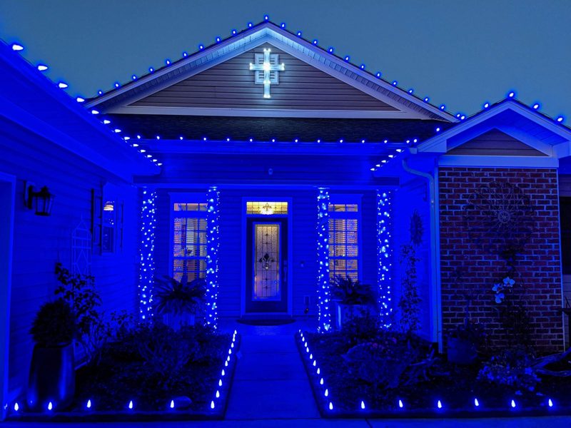 Home outlined in blue Christmas lights with a lit cross on the gable and blue-wrapped entry columns