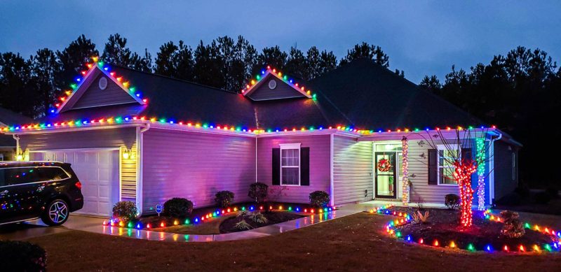 Single-story home with multicolor roofline lights and stake lighting along the driveway