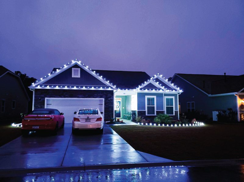 Home with warm white roofline and gable lights reflected on a wet driveway