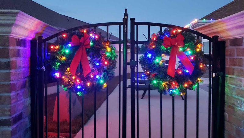 Lit wreaths with red bows on a wrought-iron entry gate