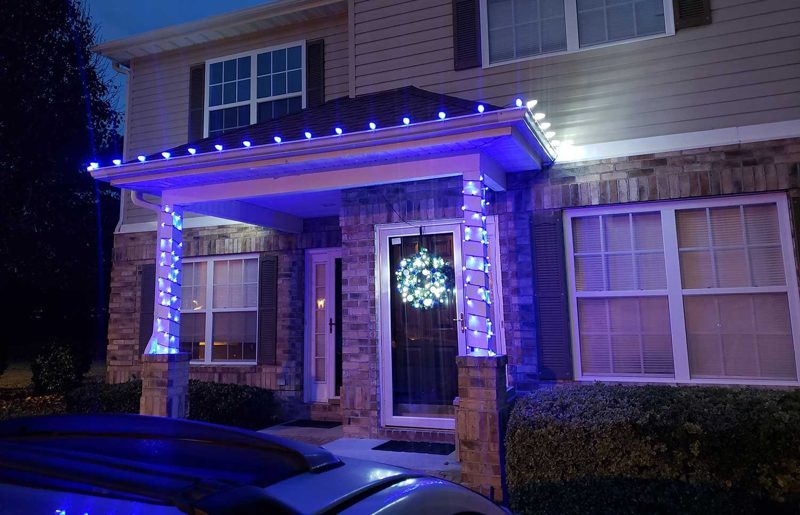 Entry columns wrapped in blue lights with a lit wreath on the front door