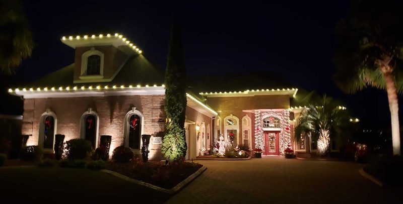 Brick home with warm white roofline lights and a lit entry at dusk