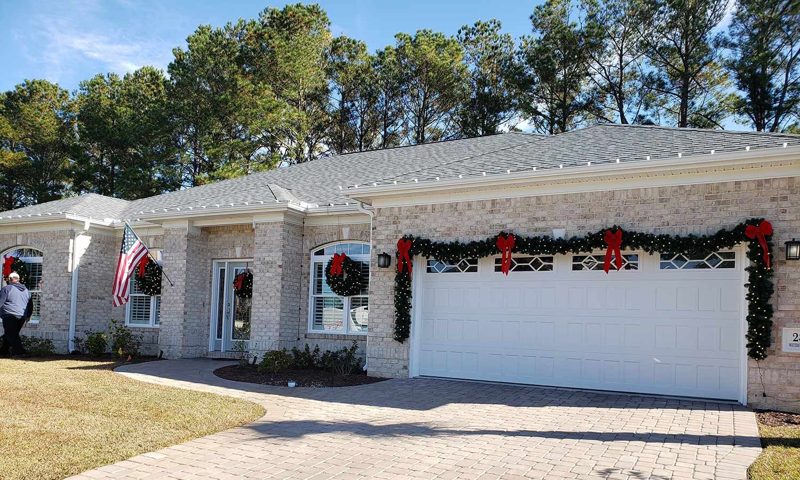 Home with lit garland and red bows over the garage and warm white roofline lights