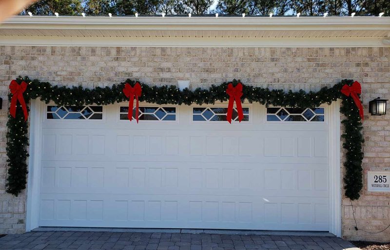 Lit garland with red bows above a garage door