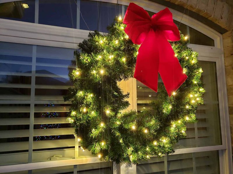 Pre-lit wreath with a red bow in a front window