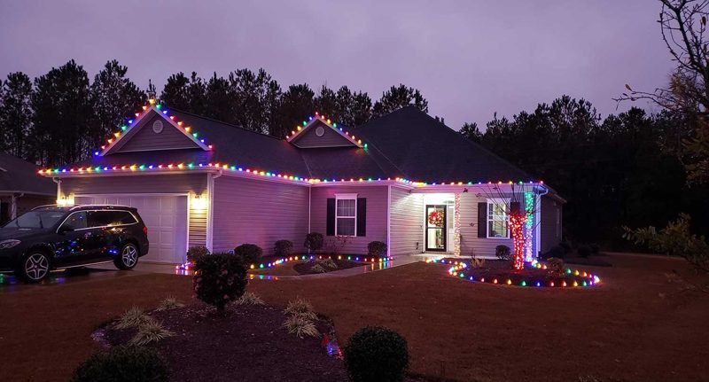 Home with multicolor roofline lights and a lit wreath