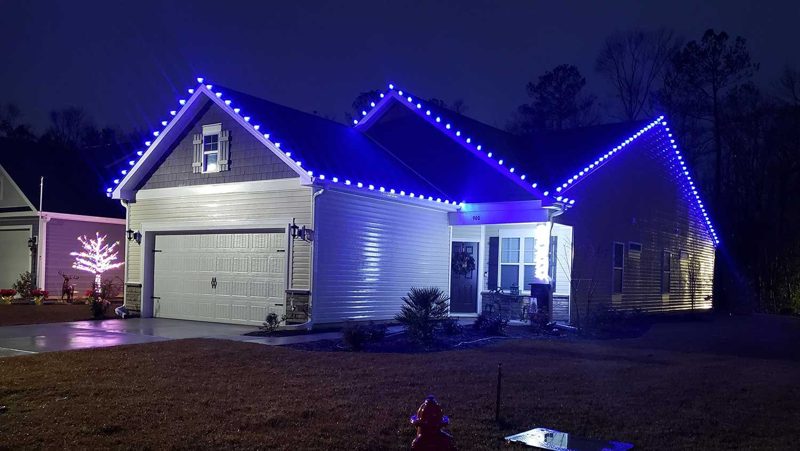 Home with blue roofline lights and lit shrubs