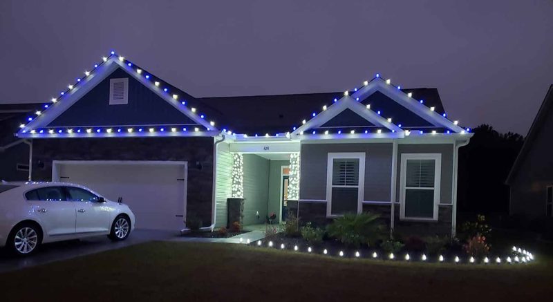 Home with warm white roofline lights and stake lighting along the drive