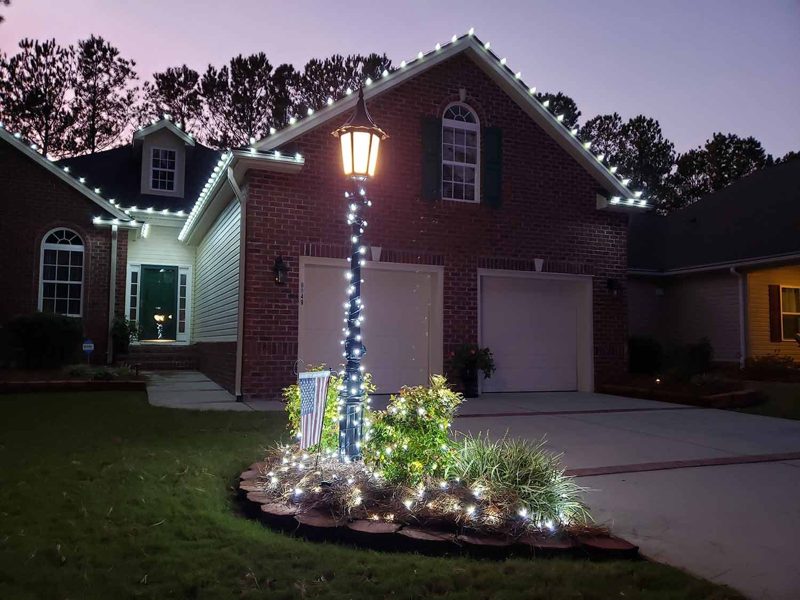 Brick home with warm white roofline lights and a lit lamp post
