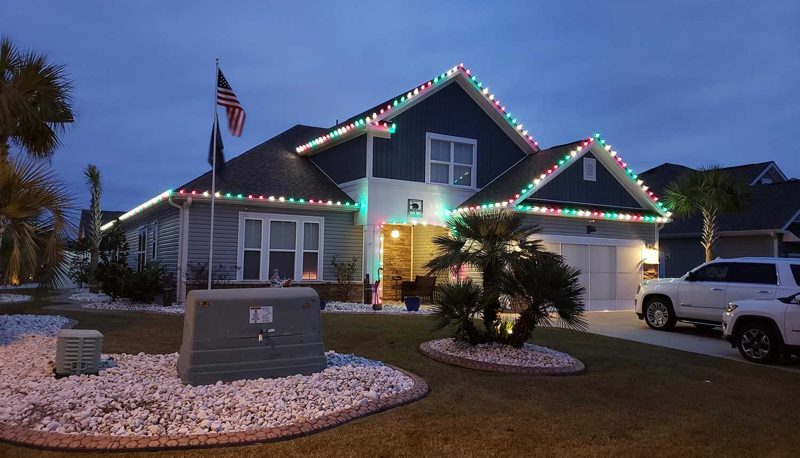 Two-story home with multicolor roofline lights and a lit palm