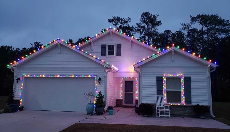 Home with multicolor roofline lights and lit wreaths on the windows