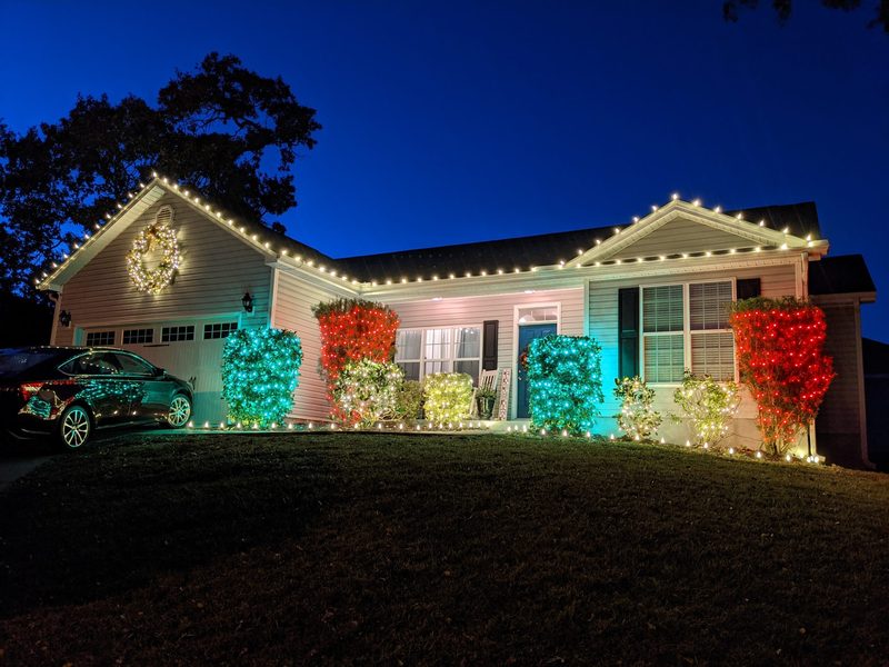 Ranch home with warm white roofline lights and colorful lit shrubs