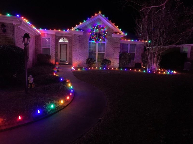 Home with multicolor roofline lights and stake lighting along the walkway