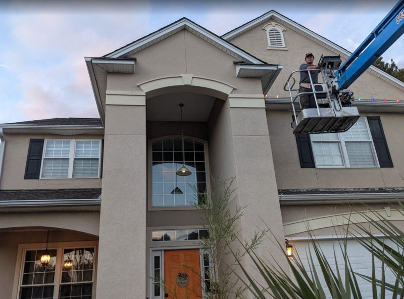 Holiday Lights by Quiet Lawn installer on a lift hanging lights on a two-story home