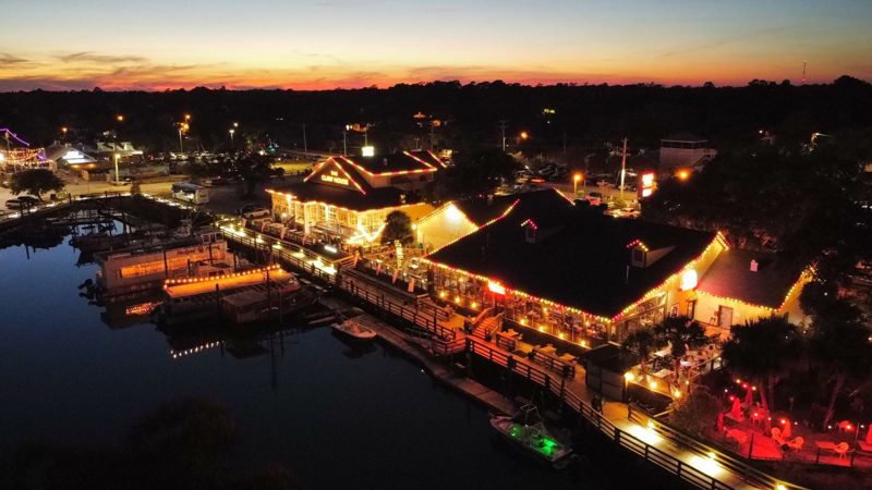 Aerial view of waterfront restaurants lit for the holidays at sunset