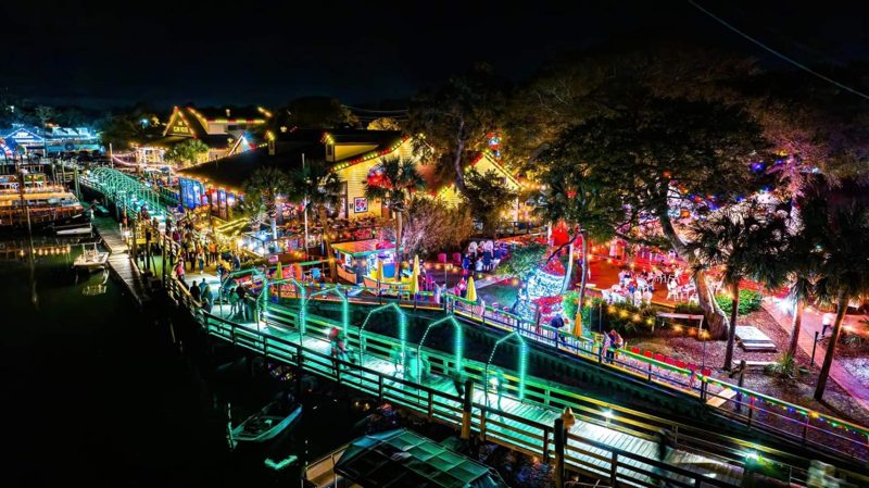 Aerial view of a waterfront boardwalk lit with holiday lights